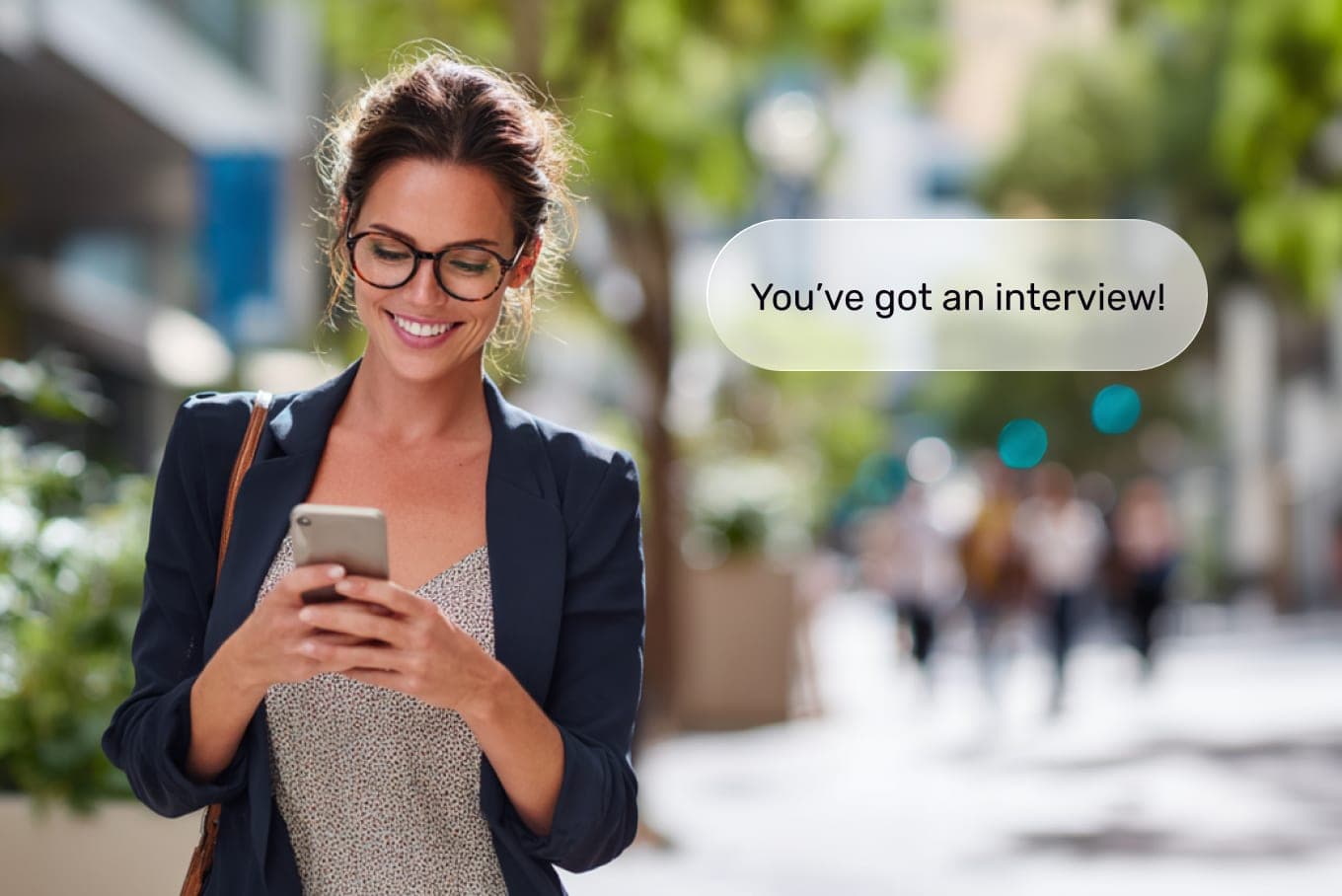 Professional woman receiving interview notification on her phone while smiling outdoors